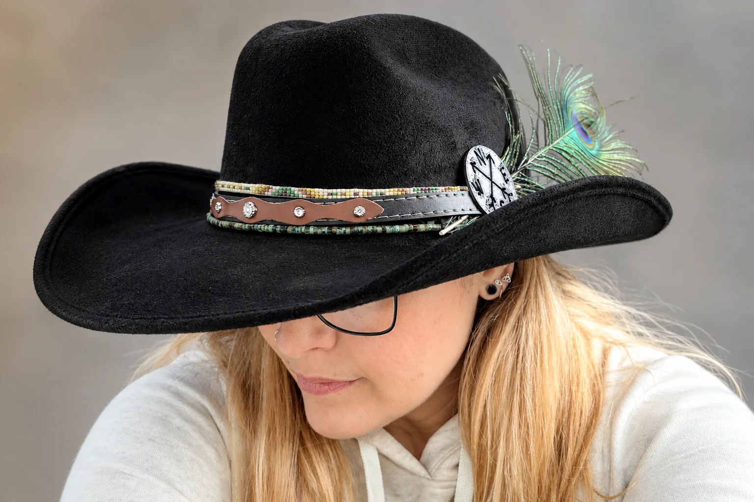 A black felt hat with a compass, beaded bands, leather strap, and peacock feather