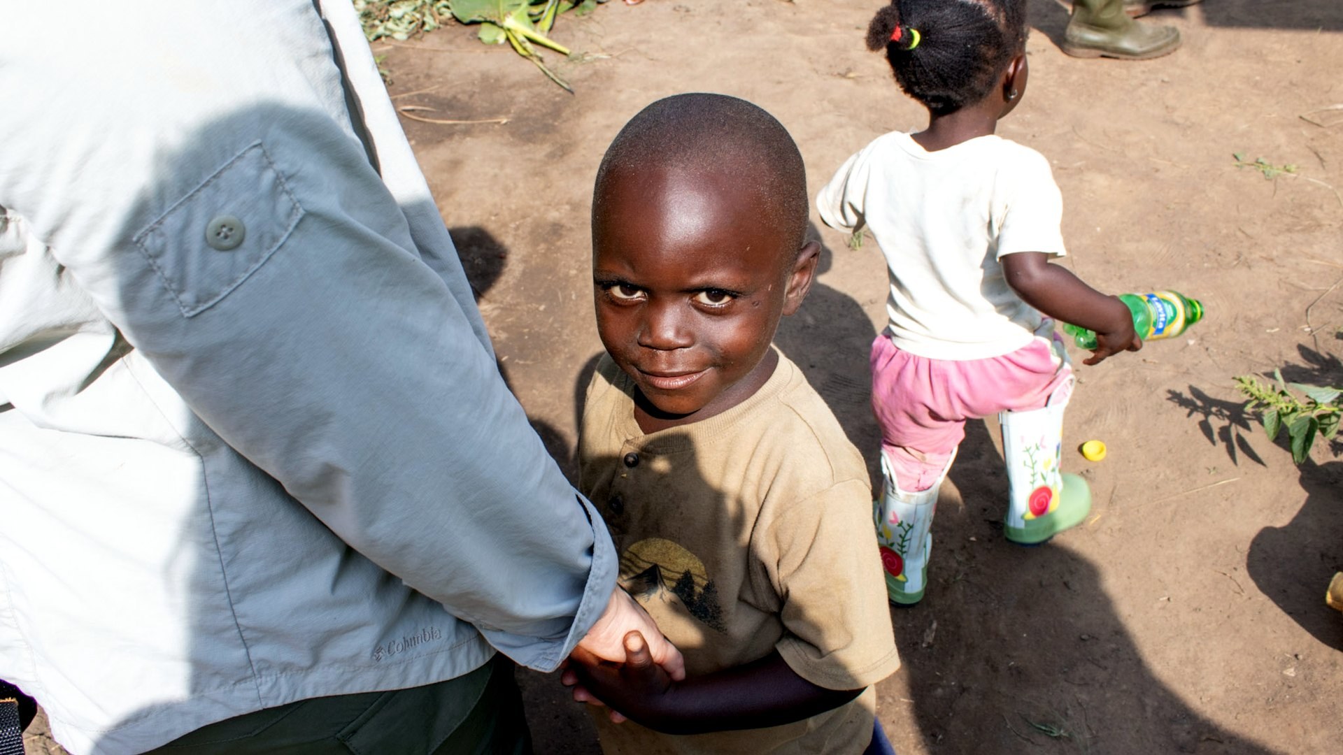 A young boy holds Janelle Nightingale’s hand and looks up at the camera during the Kobusinge planting celebration in Uganda.